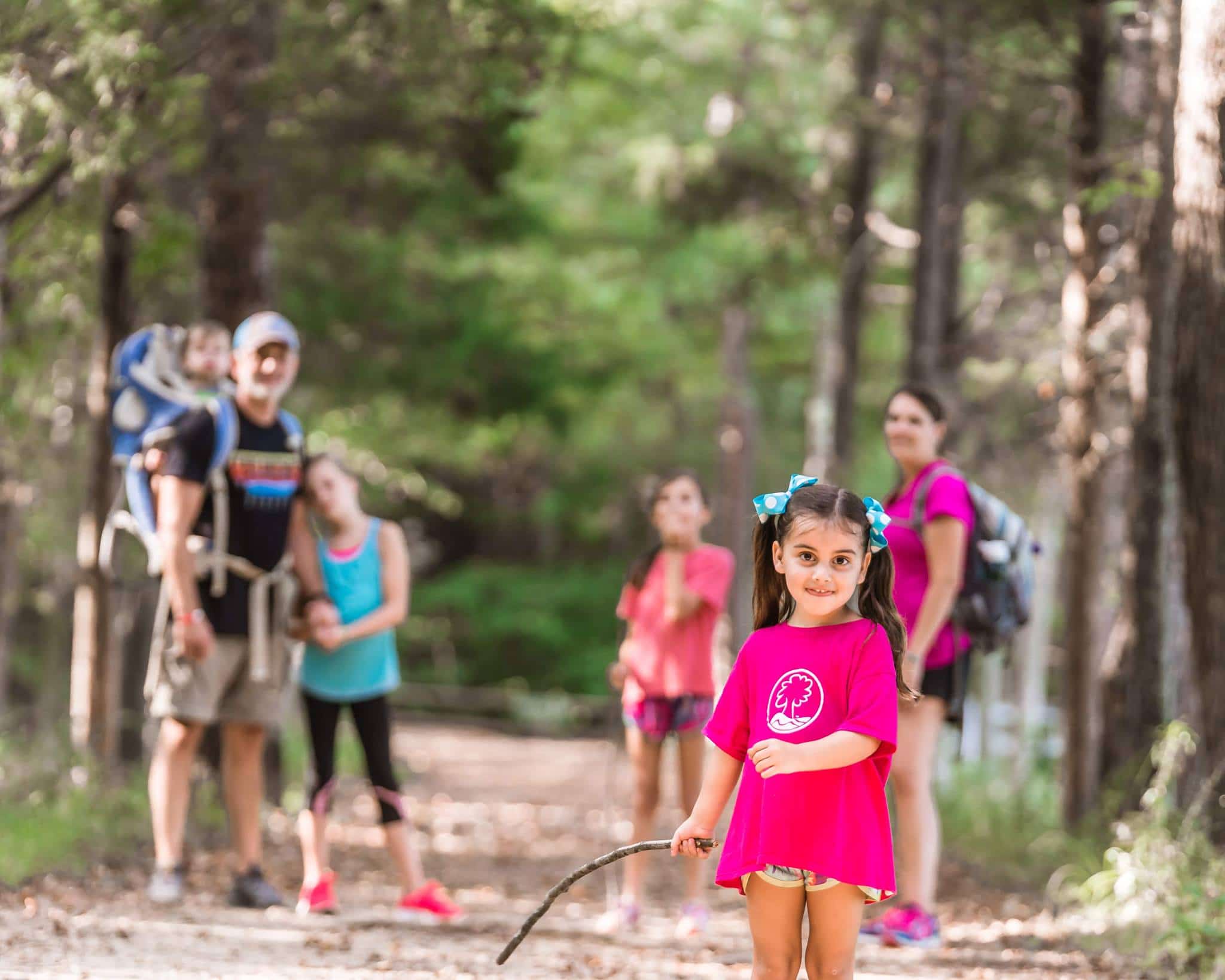 alt=Family hiking in the woods with little girl smiling