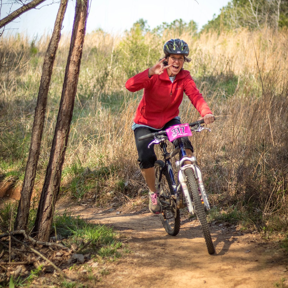 Photo of woman riding a mountain bike while smiling and making a hand signal at the camera